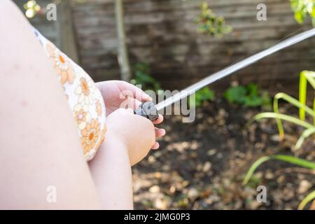 Junge Frau bewässert den Garten mit einer Schlauchleitung, bevor das Rohrleitungsverbot aufgrund von Dürre, Wasserknappheit und schlechten Niederschlägen in Kraft tritt. Stockfoto