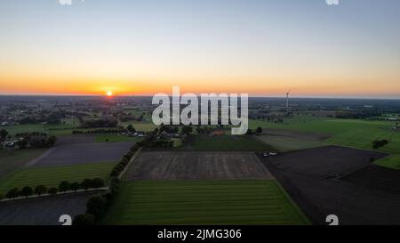 Luftaufnahme einer ländlichen Landschaft bei Sonnenaufgang in Belgien. Ländliche Farm, Maisfelder, grüne Felder, Sonnenlicht und Nebel. Belgien, Eu Stockfoto