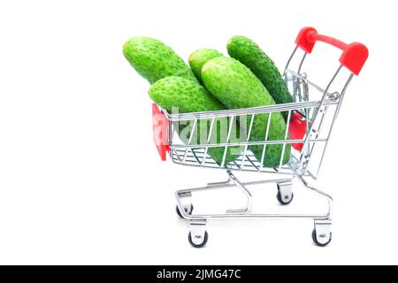Haufen frischer Gurken in einem kleinen Einkaufswagen, isoliert auf weißem Hintergrund. Online-Lieferung von frischem Gemüse und Lebensmitteln. Stockfoto