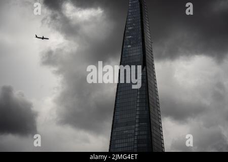 London, Großbritannien - Jun 09 2022: Der Shard bei stürmischem Wetter mit einem Flugzeug, das darauf zufliegt. Abstrakte moderne Architektur Tapete London Stockfoto