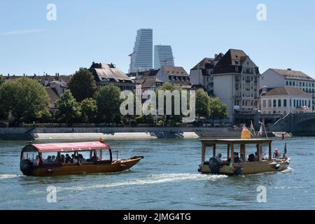 Typische kleine Wassertaxis mit Touristen, die auf dem Rhein in Basel segeln. Im Hintergrund sind beide Roche Towers, ein Schweizer multinationales Pharmaunternehmen Stockfoto