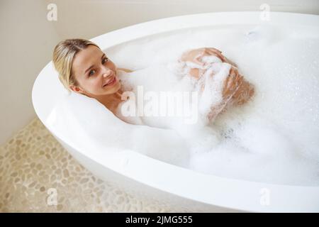 Blick von oben auf die attraktive junge Frau, die sich in der Badewanne entspannt und vor der Kamera lächelt. Stockfoto
