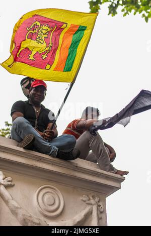 COLOMBO, SRI LANKA: 9.. Juli 2022: Zwei Demonstranten sitzen auf einer Mauer in der Chatham Street und schwenken während des Massenproteste gegen die Wirtschaftskrise die Nationalflagge. Stockfoto