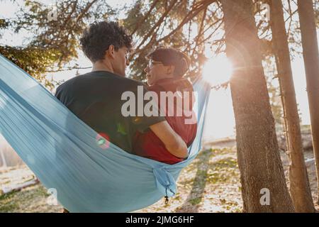 Rückansicht auf kaukasischen glücklichen Mann und Frau in der Liebe sitzt in der Hängematte im Wald und umarmt. Stockfoto