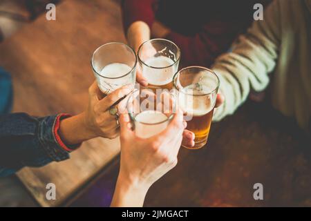 Junge Leute feiern mit Bierkröten im irish Pub - Nahaufnahme eines Hands mit Biergläsern, die über den Tisch des Pubs klirren - Freund Stockfoto