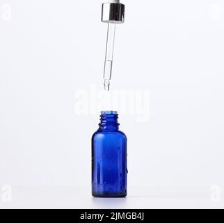 Ätherisches Öl, das aus dem bernsteinfarbenen Glasbehälter fällt. Blaue Flasche kosmetisches Öl mit einer Pipette Stockfoto