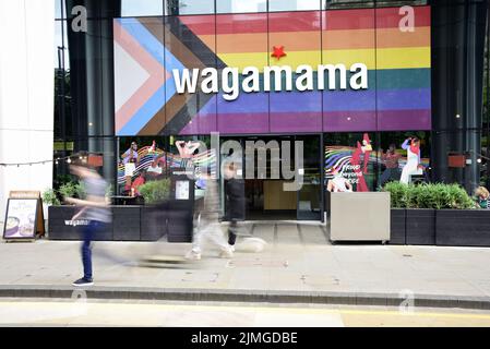 Die Menschen gehen vorbei am Restaurant Wagamama, St. Peter's Square, Manchester, Großbritannien, jetzt mit der Progress Flag an der Vorderseite. Stockfoto