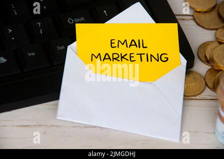 E-Mail-Marketing-Text auf gelbem Notizblock in einem Umschlag auf einem Keyboard-Computer mit Goldmünzen. Online-Geschäftskonzept Stockfoto