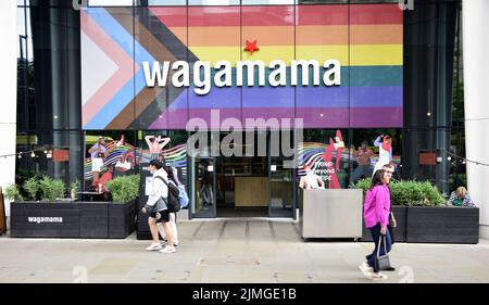 Die Menschen gehen vorbei am Restaurant Wagamama, St. Peter's Square, Manchester, Großbritannien, jetzt mit der Progress Flag an der Vorderseite. Stockfoto