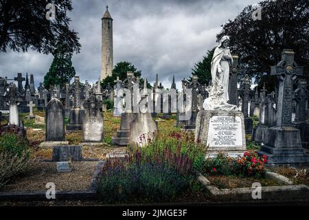 Alte Gräber und Grabsteine auf dem Friedhof von Glasnevin mit dem Round Tower, Irland Stockfoto