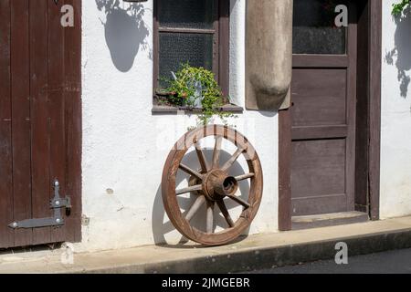 Antikes Vintage-Kutschenrad aus Holz, das an der Wand hängt. Rustikale Dekoration. Stockfoto