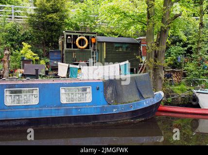 Ein altes, schmuddeliges, blaues, enges Boot, das neben Holzschuppen festgemacht ist und auf dem rochdale Kanal in der Nähe der hebdenbrücke gewaschen wird Stockfoto