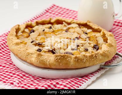 Gebackener runder Kuchen mit Apfelstücken, bestreut mit Mandelflocken auf einem weißen Tisch Stockfoto