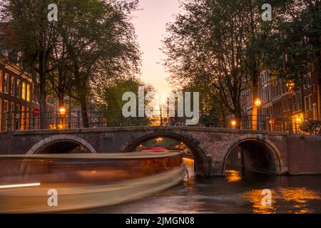 Sonnenuntergang auf dem Amsterdamer Kanal und ein Boot unter der Brücke Stockfoto