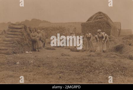 Mitglieder der Landarmee der Frauen auf einem Bauernhof, die während des Ersten Weltkriegs die Ernte einbrachten. Die uniformierten Frauen binden Heurollen, und im Hintergrund ist ein Heustapel zu sehen. Ein Mann mit flacher Mütze beobachtet. Der Stempel des Fotografen - Frederick Joseph Seaman von Doncaster - ist in der rechten unteren Ecke zu sehen. Stockfoto