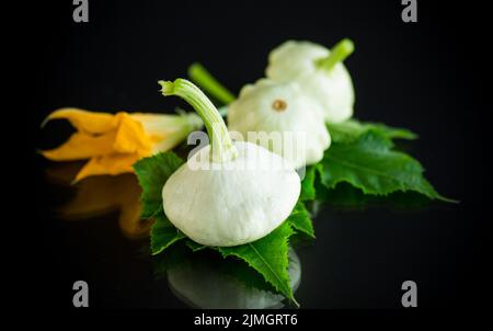 Frischer Bio-Kürbis mit Blumen und Laub isoliert auf schwarzem Hintergrund Stockfoto