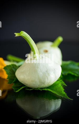 Frischer Bio-Kürbis mit Blumen und Laub isoliert auf schwarzem Hintergrund Stockfoto