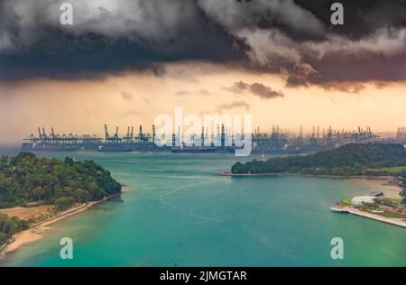 Der riesige verkehrsreichste Logistikhafen in Singapur, viele Krane, um Container zu bewegen, riesige Frachtschiffe im Hintergrund, Wolkenkratzer Stockfoto