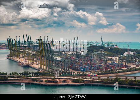 Der riesige verkehrsreichste Logistikhafen in Singapur, viele Krane, um Container zu bewegen, riesige Frachtschiffe im Hintergrund, Wolkenkratzer Stockfoto