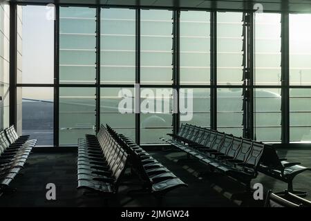 Ein verlassener Flughafen, leere Bänke durch ein Panoramafenster, ein riesiges Flugzeug, das durch die Glaswände eines Knotenpunkts in t sichtbar ist Stockfoto