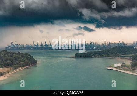 Der riesige verkehrsreichste Logistikhafen in Singapur, viele Krane, um Container zu bewegen, riesige Frachtschiffe im Hintergrund, Wolkenkratzer Stockfoto