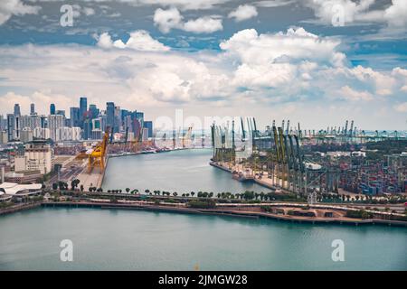 Der riesige verkehrsreichste Logistikhafen in Singapur, viele Krane, um Container zu bewegen, riesige Frachtschiffe im Hintergrund, Wolkenkratzer Stockfoto