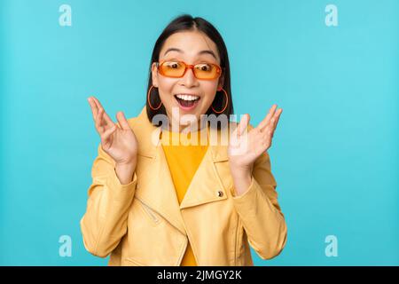 Bild einer enthusiastischen jungen asiatischen Frau, die feiert, triumphiert, überrascht und glücklich aussieht, zufrieden die Hände klatscht, steht Stockfoto