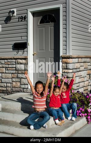 Drei indianische Mädchen im Grundschulalter, die Cousins sind, heben während der Spielzeit die Arme, während sie auf Stufen sitzen Stockfoto