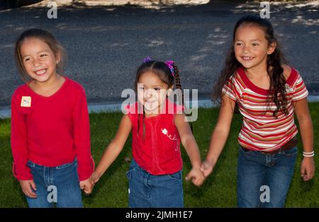 Drei indianische Mädchen im Grundschulalter, die Freunde und Schwester sind, halten sich beim Spielen die Hände. Stockfoto