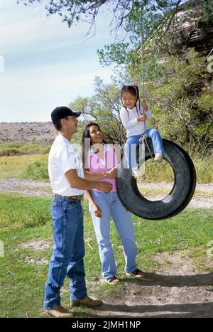 Die indianische Familie aus Vater und Mutter mit ihrer jungen Tochter spielt mit einer Reifenschaukel in ihrem Hinterhof zusammen Stockfoto