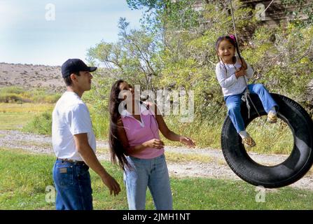 Die indianische Familie aus Vater und Mutter mit ihrer jungen Tochter spielt mit einer Reifenschaukel in ihrem Hinterhof zusammen Stockfoto