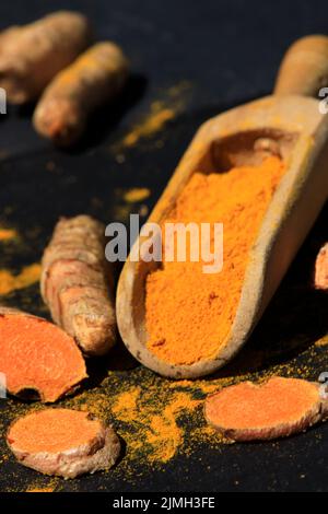 Kurkuma Pulver in einem Holzlöffel und Wurzeln auf einem dunklen Tisch (Curcuma longa), Kurkuma Stockfoto