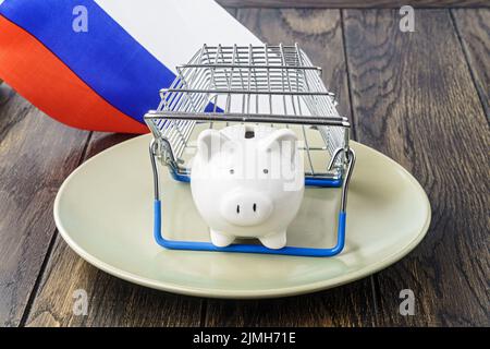 Sparschwein auf dem Teller unter dem Korb und der russischen Flagge. Konzept der Handelsinflation Stockfoto