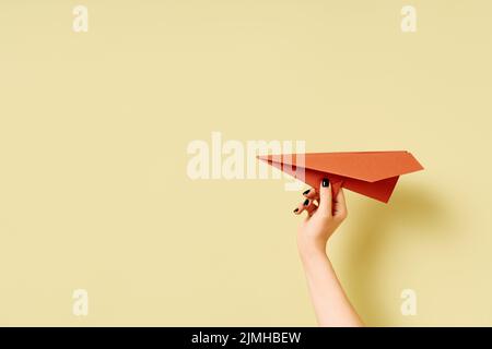 Die Hand einer Frau hält ein Flugzeug aus Terrakotta-Papier auf olivgrünem Hintergrund Stockfoto