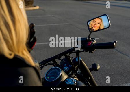 Ein schönes blondes Model genießt das Wetter im Freien, während sie mit ihrem Motorrad posiert Stockfoto