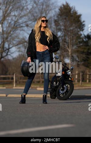 Ein schönes blondes Model genießt das Wetter im Freien, während sie mit ihrem Motorrad posiert Stockfoto