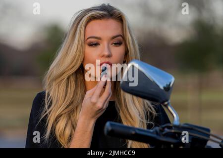 Ein schönes blondes Model genießt das Wetter im Freien, während sie mit ihrem Motorrad posiert Stockfoto