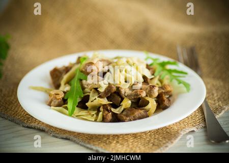 Hausgemachte gekochte Nudeln mit Fleisch und Auberginen auf einem Teller auf einem Holztisch Stockfoto