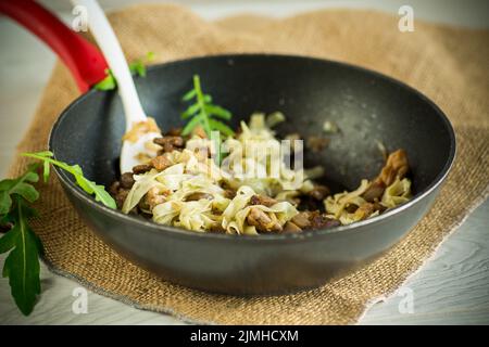 Hausgemachte gekochte Nudeln mit Fleisch und Auberginen in einer Pfanne auf einem Holztisch Stockfoto