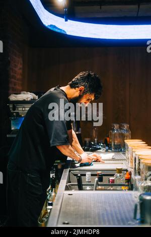 Junger kaukasischer Mann, asiatischer Bistro-Mitarbeiter, der auf der Theke den Tisch von Keimen und Staub reinigte. Stockfoto