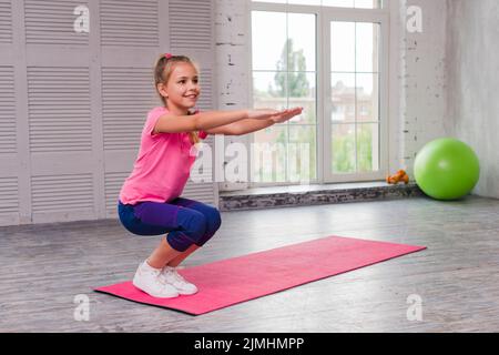 Lächelndes Mädchen hocken Ausübung rosa Matte Stockfoto