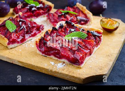 Der traditionelle deutsche Zwetschgenkuchen mit geschnittenen Pflaumen diente als Nahaufnahme auf einem rustikalen Holzbrett Stockfoto