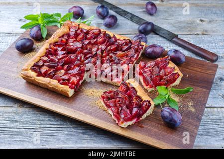 Der traditionelle deutsche Zwetschgenkuchen mit geschnittenen Pflaumen diente als Nahaufnahme auf einem Holzbrett Stockfoto