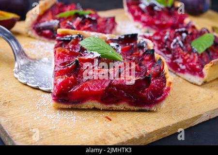 Der traditionelle deutsche Zwetschgenkuchen mit geschnittenen Pflaumen diente als Nahaufnahme auf einem rustikalen Holzbrett Stockfoto