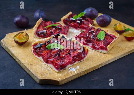 Der traditionelle deutsche Zwetschgenkuchen mit geschnittenen Pflaumen diente als Nahaufnahme auf einem rustikalen Holzbrett Stockfoto