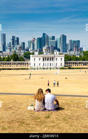 6. August 2022 - London, Großbritannien - Paar sitzt auf ausgetrocknetem Grasland im Greenwich Park nach einer Reihe von Hitzewellen und Rekordtemperaturen, der Stadt mit Dürre und Wasserrationierungsmaßnahmen konfrontiert Stockfoto