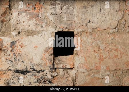 Alte rote Ziegelmauer mit einem schwarzen Loch in der Mitte. Der texturierte Hintergrund einer alten Ziegelwand. Für die Innenraumgestaltung kann ein Panoramablick auf eine leere Wand mit Kopierraum genutzt werden. Stockfoto