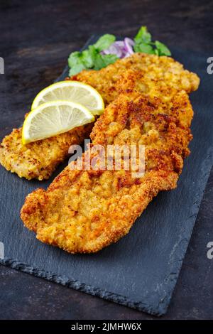 Traditionelles frittiertes Schnitzel mit Zitronenscheiben und Zwiebelringen, das als Nahaufnahme auf einem schwarzen Tablett serviert wurde Stockfoto