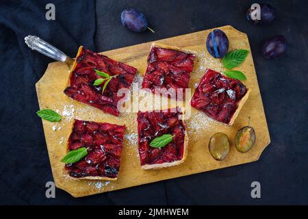 Traditionelle deutsche Zwetschgenkuchen mit geschnittenen Pflaumen dienten als Draufsicht auf einem rustikalen Holzbrett Stockfoto