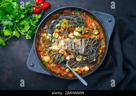 Traditionelle italienische Spaghetti al nero di seppia mit Tintenfisch-Tinte in Tomatensauce serviert als Draufsicht in einer gusseisernen Pfanne auf einer R Stockfoto